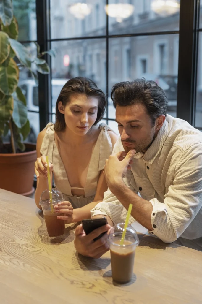 casal em um restaurante, ambos olhando para seus celulares.